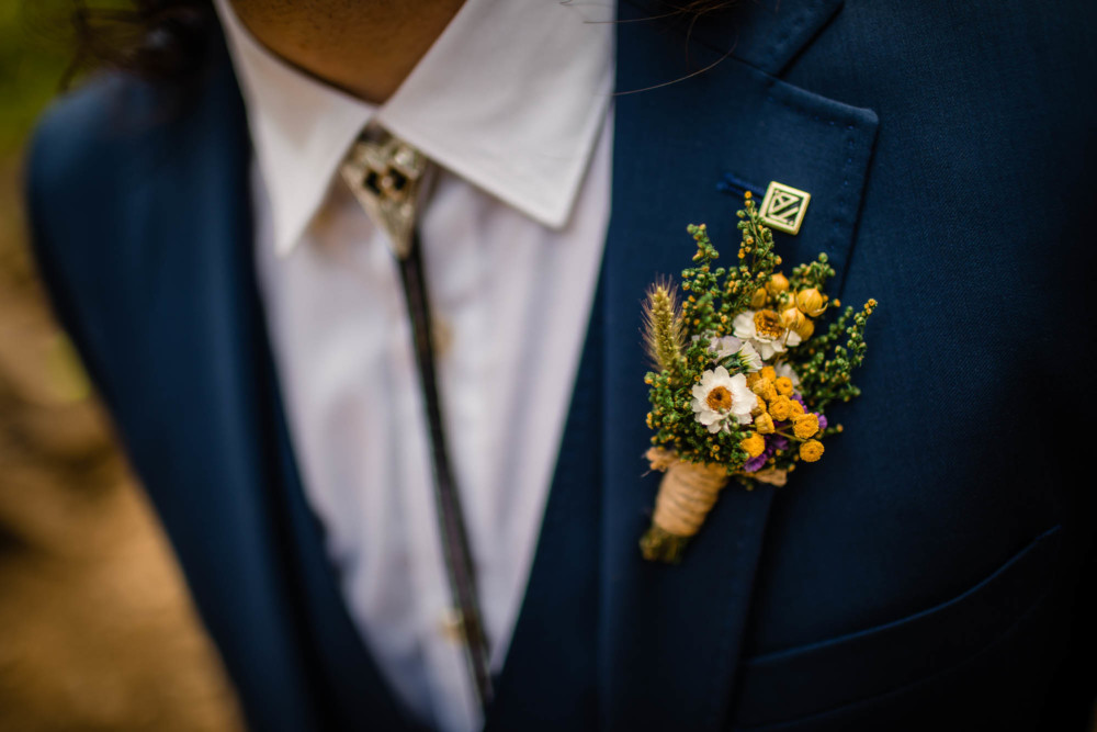 Detail of grooms boutonniere made of wildflowers and his bolo tie