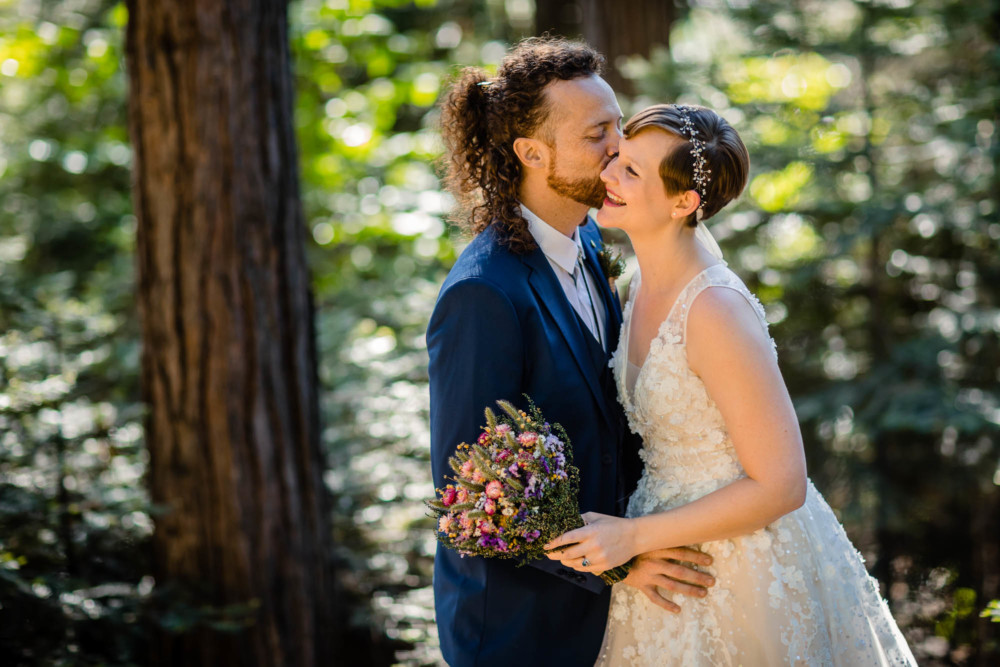 Groom kissing a bride on the cheek in a forest at Paradise springs near yosemite national park