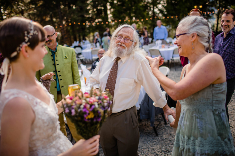 Gray haired, bearded man gestures during a conversation at a wedding reception in the mountains