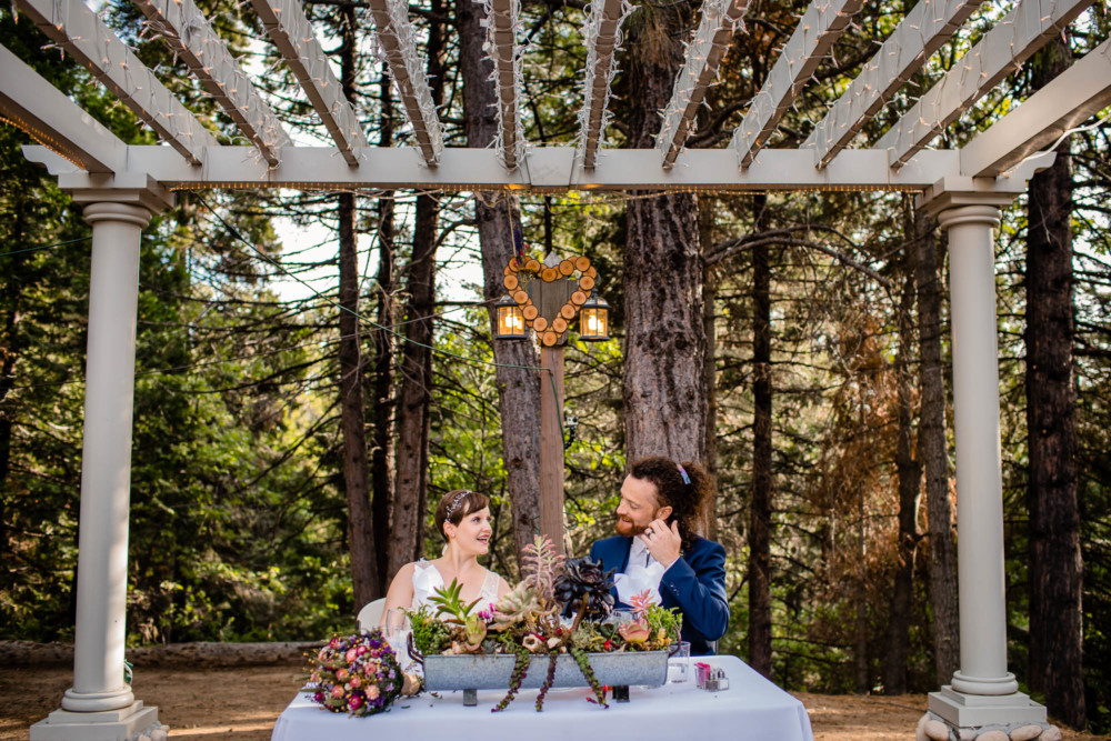 Bride and groom sit at their sweetheart table at their wedding reception in the mountains at Paradise Springs