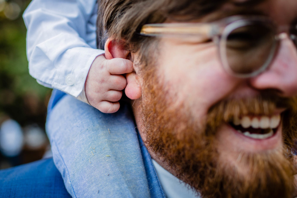 toddler sticks his fingers in his dad's ears to hold on