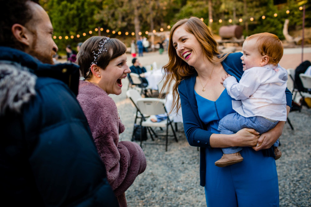 Bride and baby laugh at each other at a wedding reception in the mountains