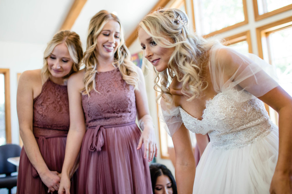 Bridesmaids look on and smile as the bride adjusts her dress