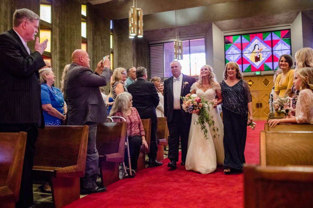 Mother and father of the bride walk their daughter down the aisle in multi colored St Anthony's Catholic Church