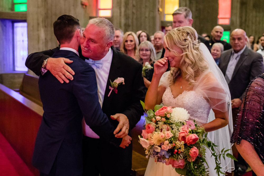 Father of the bride gives the groom a hug as he hands of his daughter the bride