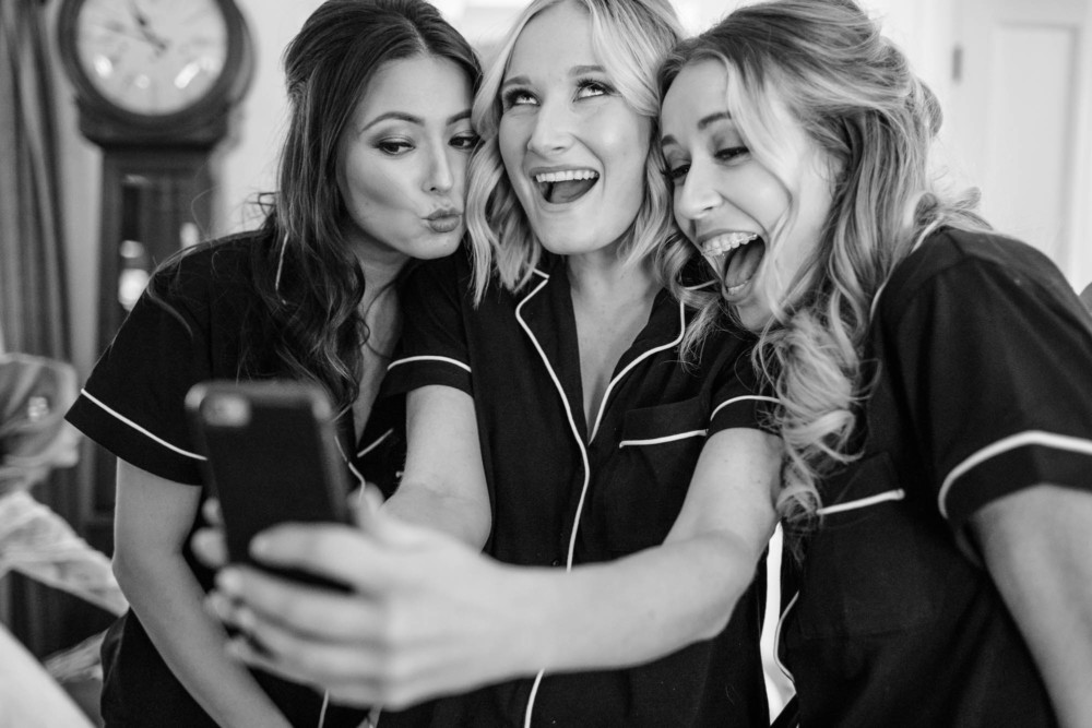 Bridesmaids taking a silly selfie while doing hair and makeup before the wedding