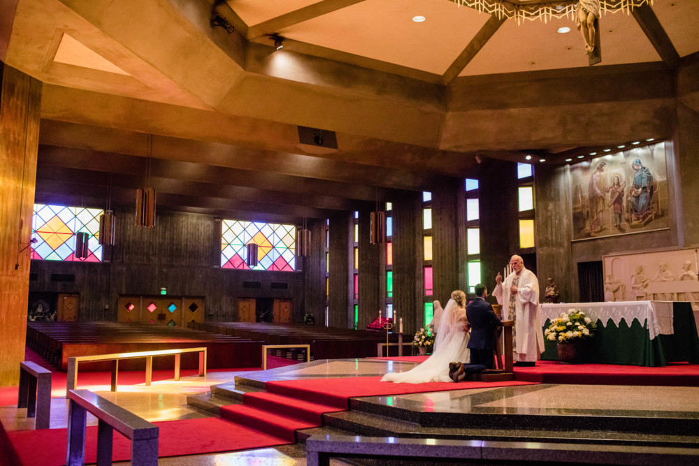 Wide photograph of a bride and groom in the multicolored interior of St Anthony's Catholic Church in Fresno, CA