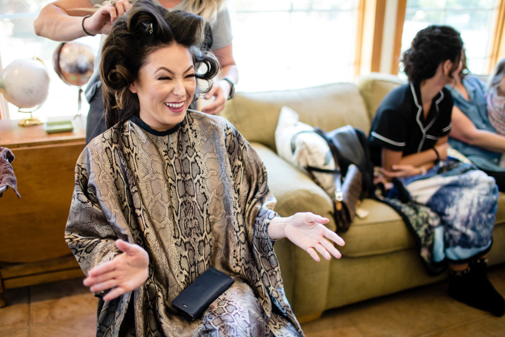 Bridesmaid with large curler's in her hair laughs and gestures while getting ready for the wedding