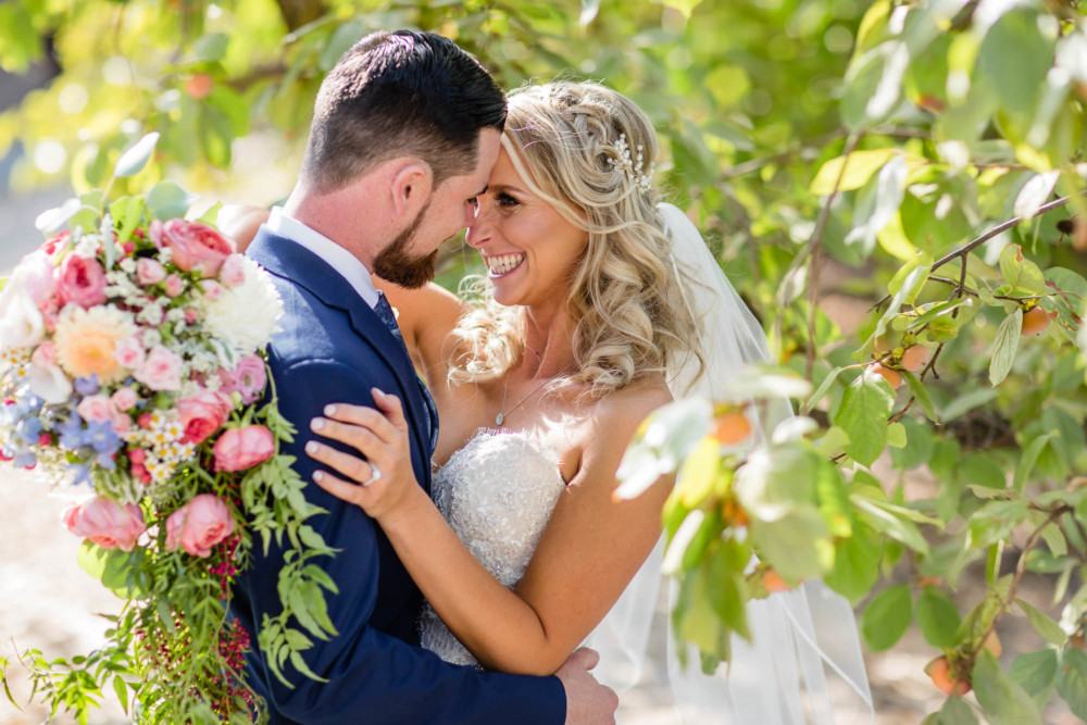 bride and groom nuzzle among the leaves of a fruit tree