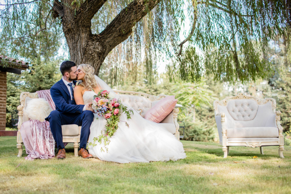 Portrait of bride and groom on a vintage couch under a willow tree