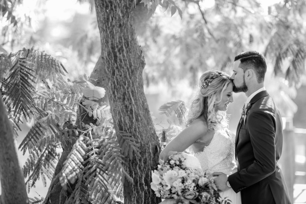 Groom kisses the forehead of the bride in black and white