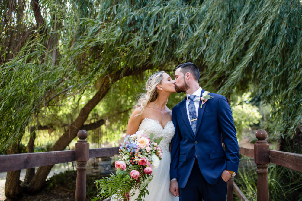Portrait of bride and groom kissing in front of a willow tree