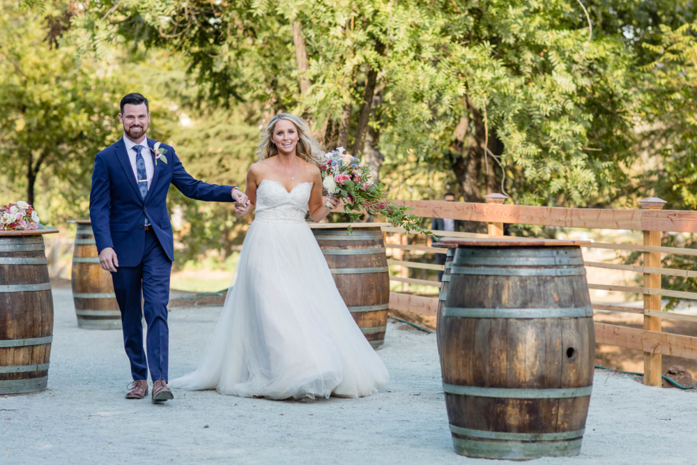 Bride and groom enter their wedding reception past some decorative barrels
