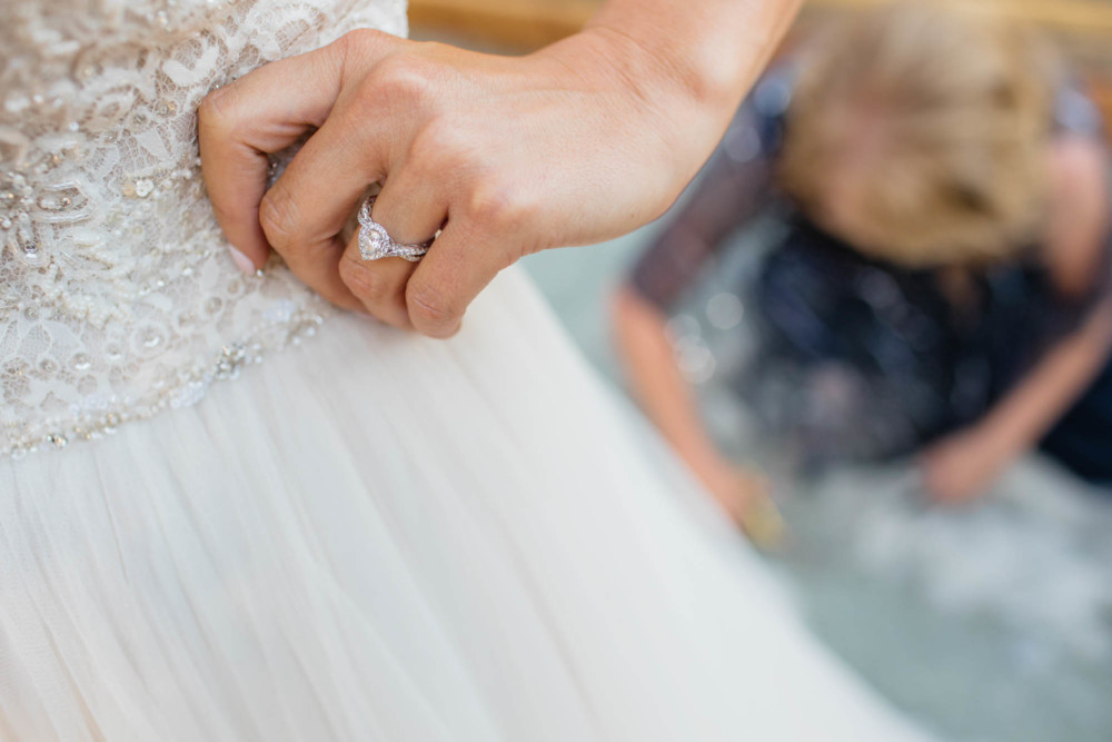 Detail of brides ring while her mother cuts off the bottom of her dress
