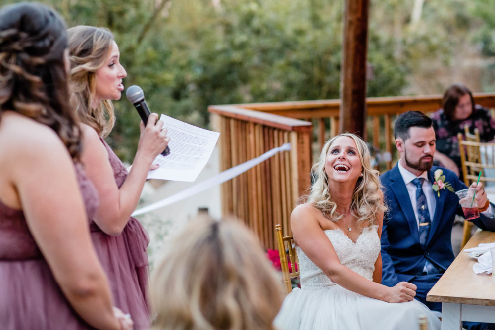 bride reacts with laughter during her sisters speech at the wedding reception