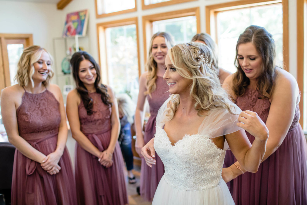 Bridesmaids react to the bride showing off her wedding dress before her wedding in Fresno, CA