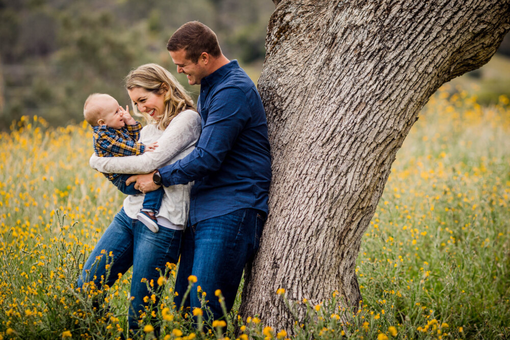 Mother and father laughing and interacting with their baby on a grassy hillside foothill