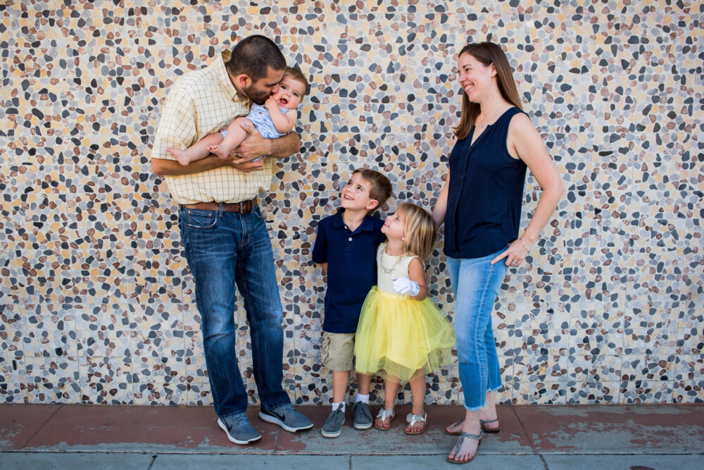 Family with three children laugh in front of a colorful mosaic wall