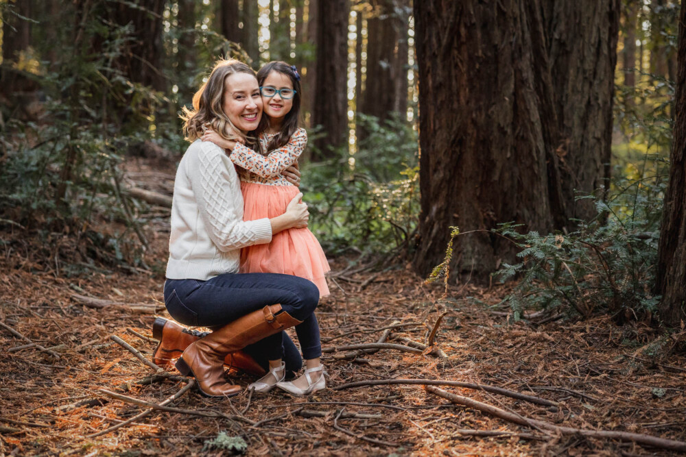 Mother and daughter embrace and cuddle among the redwoods in the forest