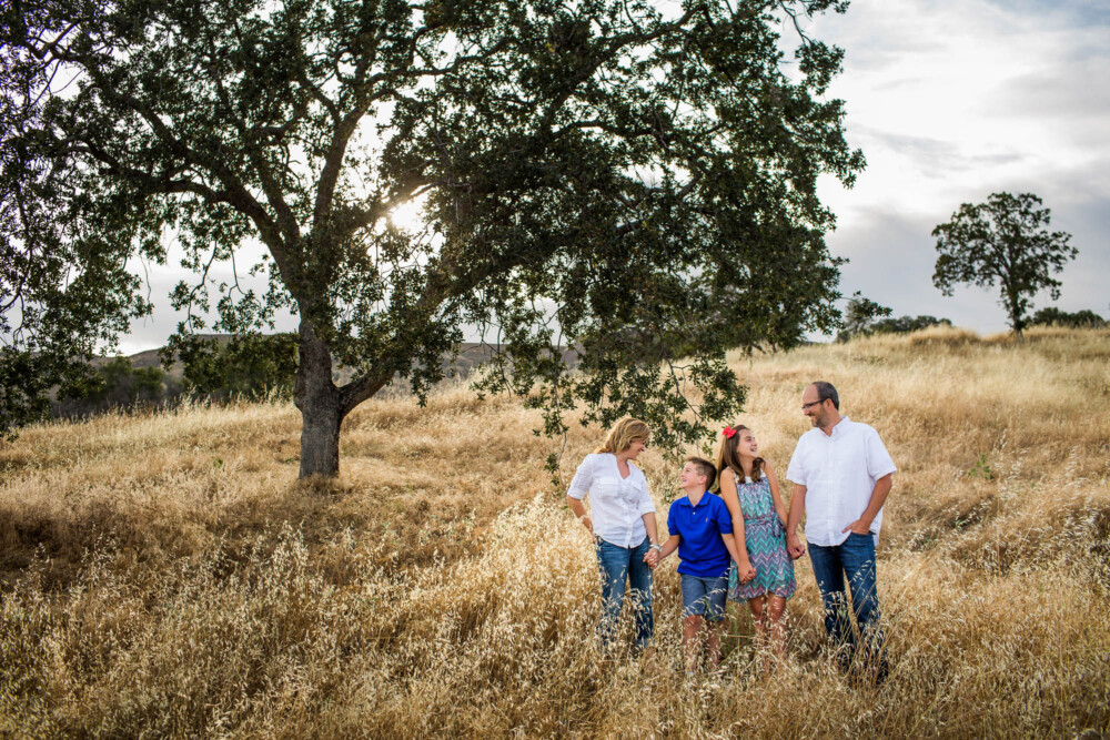 Family with teen kids on a golden grassy hill side under an oak tree