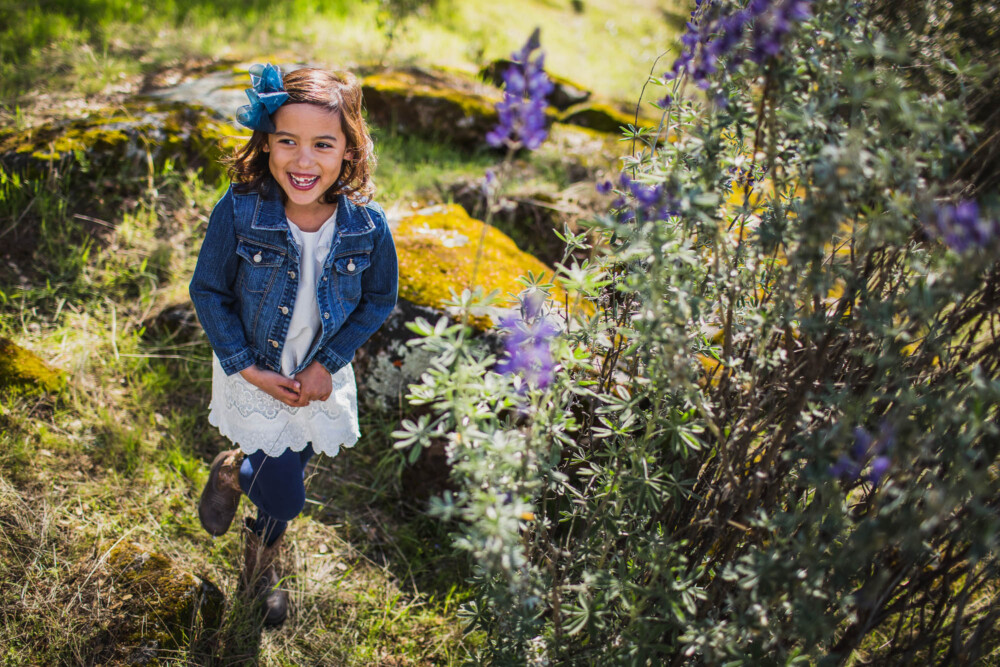 Girl laughing and dancing next to a purple lupine bush