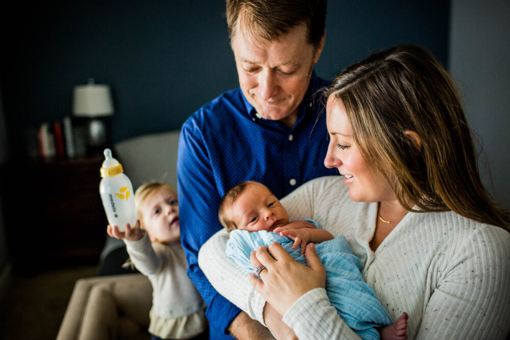 Mother and father hold their newborn while an older child offers them a bottle for the baby