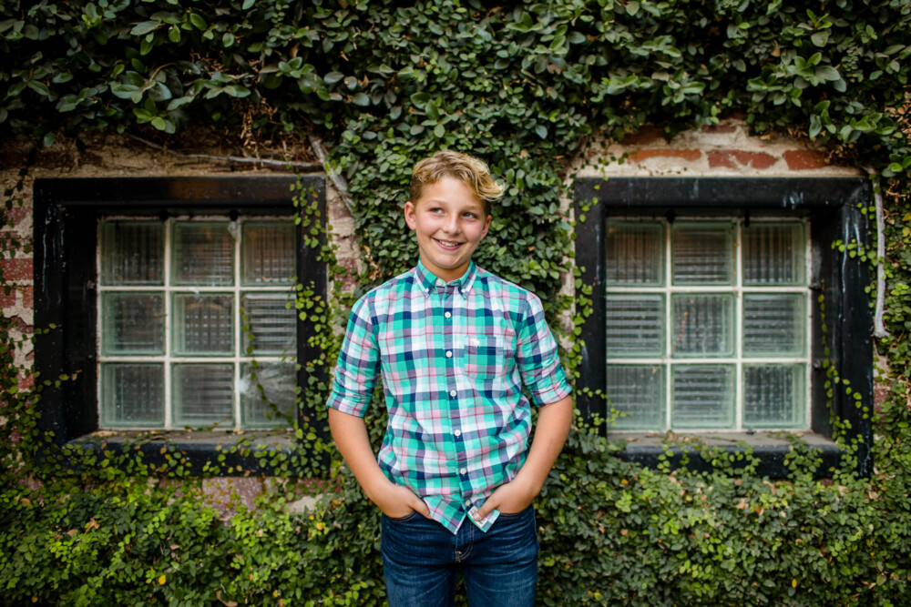 Teen boy stands and smiles in front of an ivy covered wall