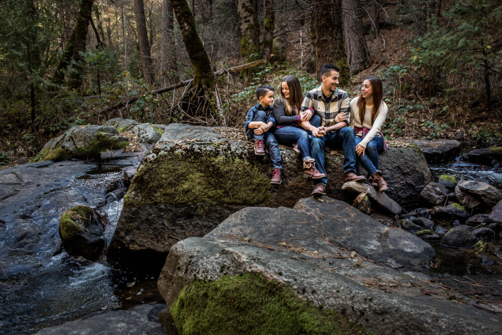 Family sits on a large granite boulder next to a mountain creek in a forest