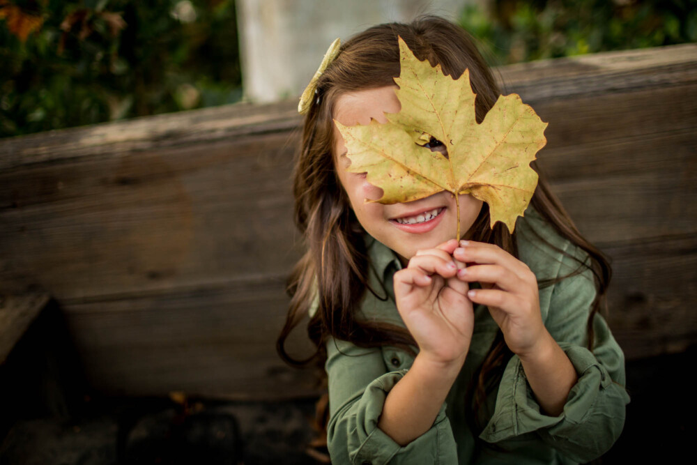 Young girl peeking through a hole in a large leaf