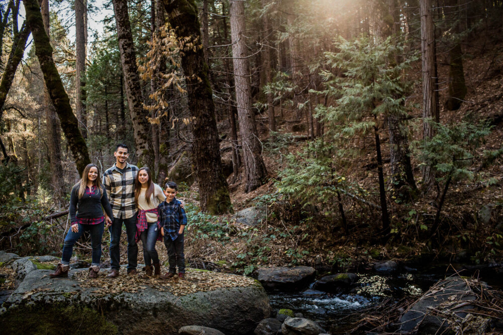 Family poses for a family portrait on a large granite rock in the middle of a creek
